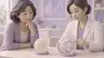 Respectful clay-render scene of a middle-aged East Asian woman and a female clinician examining two abstract translucent breast-tissue models with different densities on a consultation table; soft lavender and cream palette, no labels, text, words or logos.