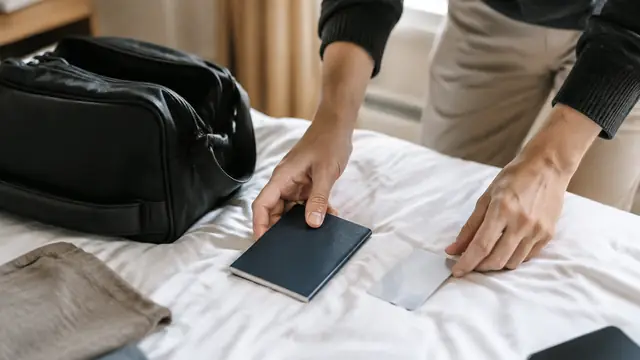 Traveler arranging a closed plain passport holder and a face-down identification card beside a small travel bag, with no visible text or logos.
