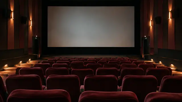 Empty cinema auditorium with plush seats facing a large blank screen, illuminated by subtle aisle lighting.