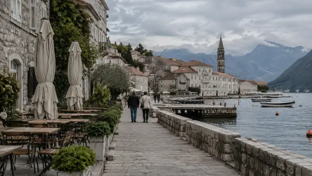 A quiet coastal town in early autumn with a few pedestrians, closed plain cafe umbrellas and overcast skies.