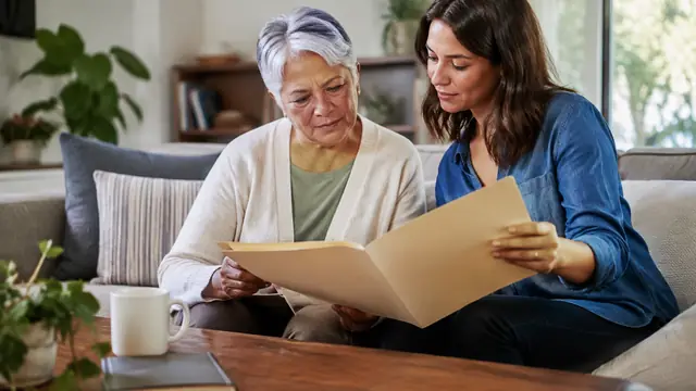 An older adult reviews blank folders with a trusted family member at home, with no visible text, logos, brand names or readable screens.